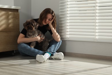 Photo of Sad young woman and her dog sitting on floor indoors, space for text