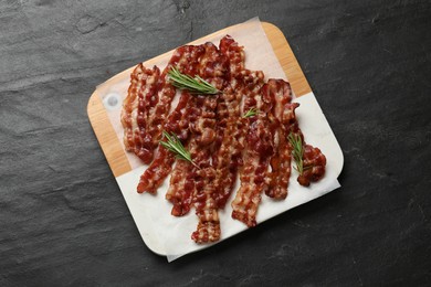 Photo of Slices of tasty fried bacon and rosemary on black table, top view