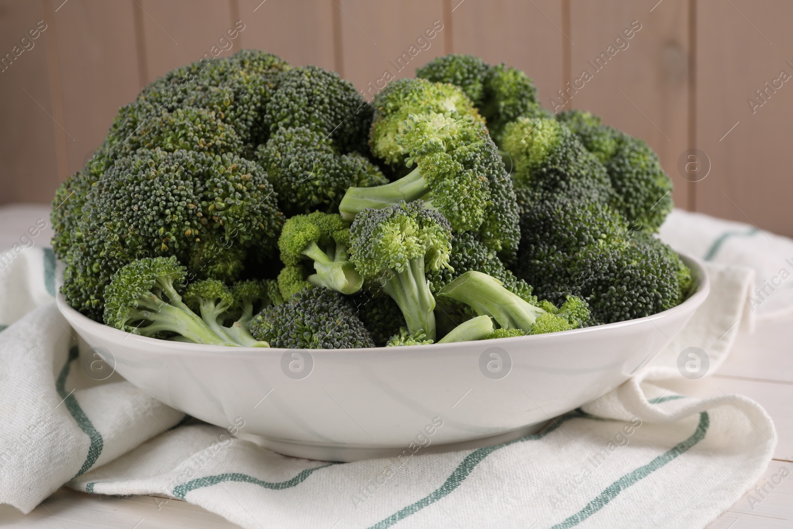 Photo of Bowl of fresh raw broccoli on white wooden table, closeup