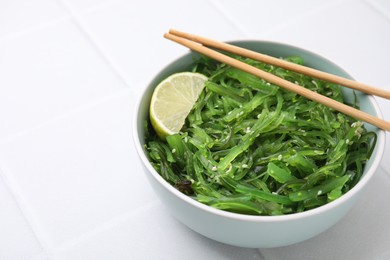 Photo of Tasty seaweed salad in bowl served on white tiled table, closeup