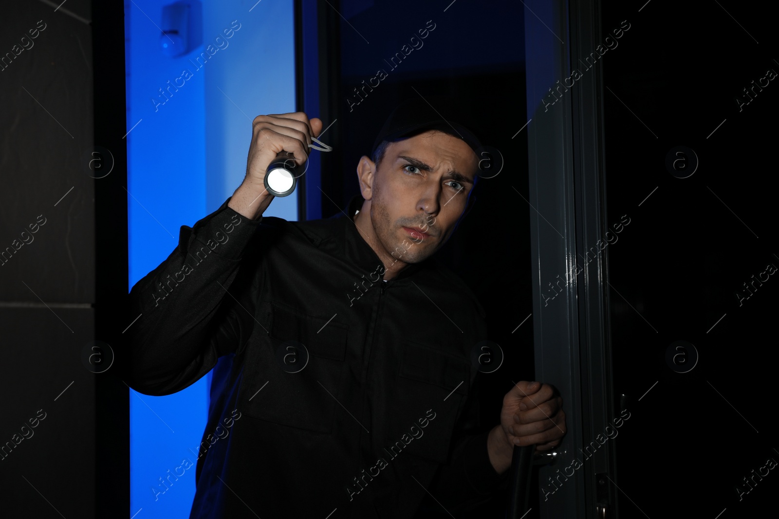 Photo of Male security guard with flashlight near entrance door at night