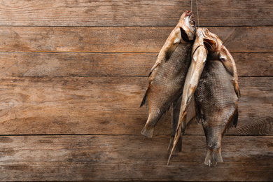 Photo of Dried fish hanging on rope against wooden background, space for text