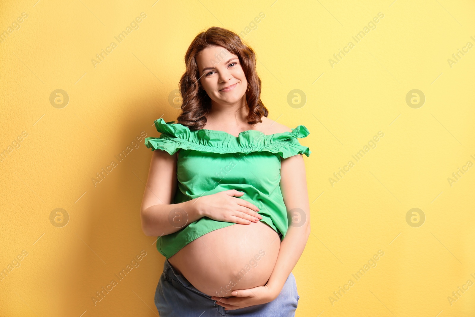 Photo of Young pregnant woman in casual clothes on color background