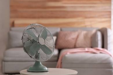Photo of Modern electric fan on white table in living room. Space for text