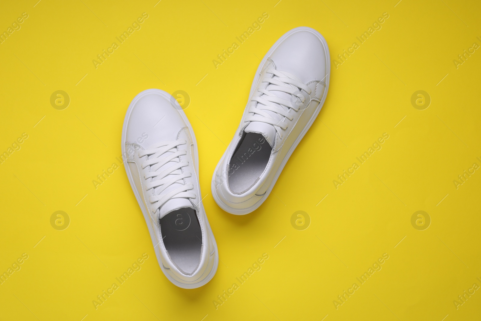 Photo of Pair of stylish white sneakers on yellow background, top view