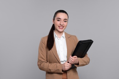 Happy real estate agent with leather portfolio on grey background