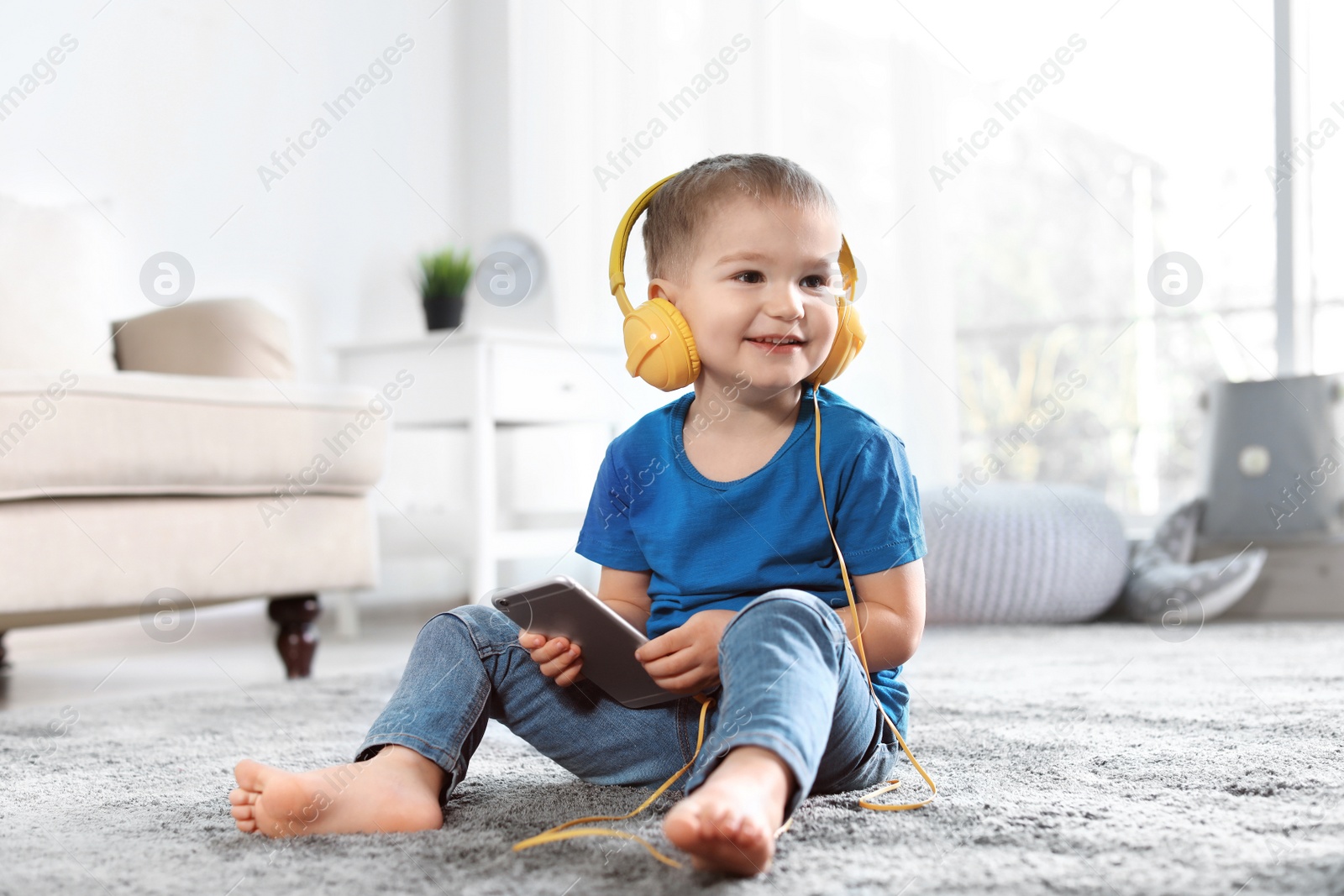 Photo of Cute child with headphones and mobile phone on floor indoors