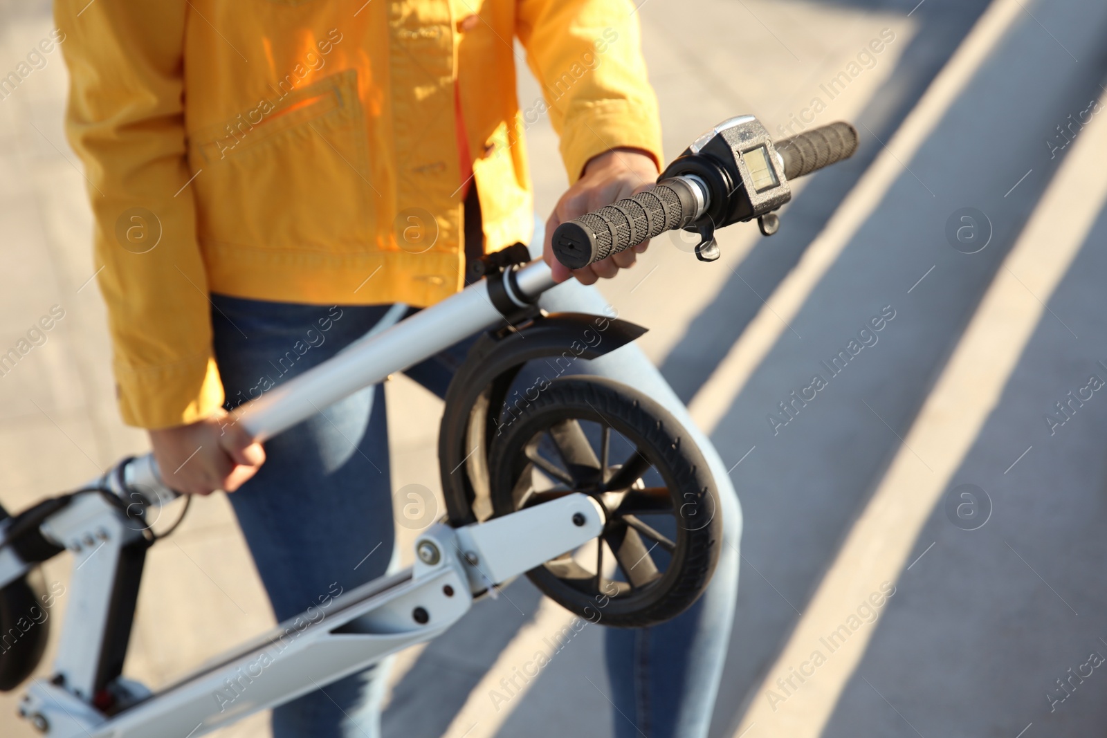 Photo of Woman carrying folded electric kick scooter outdoors, closeup