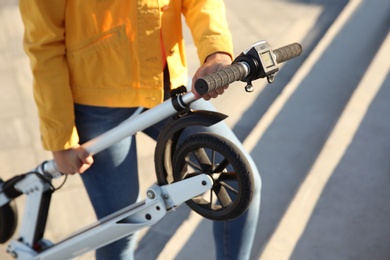 Photo of Woman carrying folded electric kick scooter outdoors, closeup