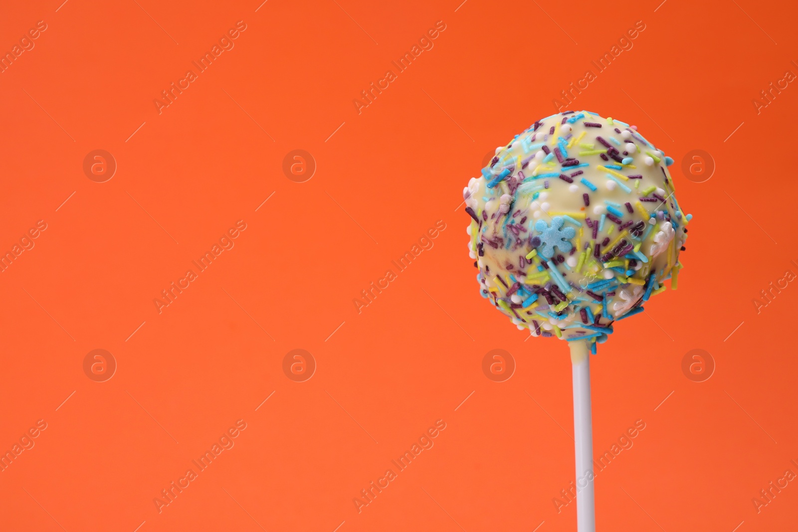 Photo of Delicious confectionery. Sweet cake pop decorated with sprinkles on orange background, closeup. Space for text