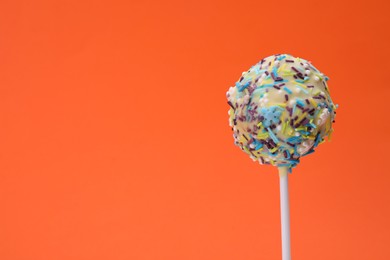 Delicious confectionery. Sweet cake pop decorated with sprinkles on orange background, closeup. Space for text