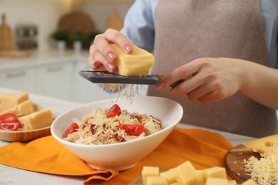 Photo of Woman grating cheese onto delicious pasta at white table in kitchen, closeup