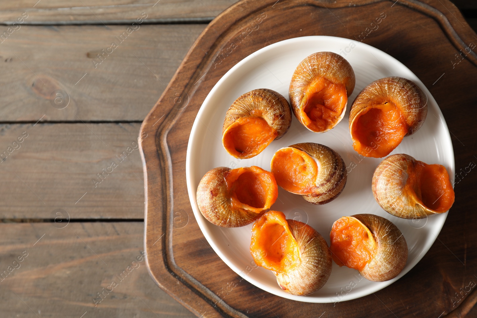 Photo of Delicious cooked snails on wooden table, top view. Space for text