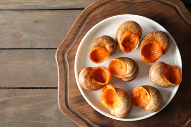 Photo of Delicious cooked snails on wooden table, top view. Space for text