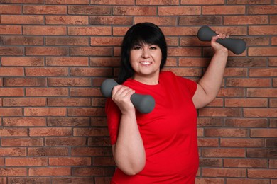 Photo of Happy overweight mature woman doing exercise with dumbbells near brick wall