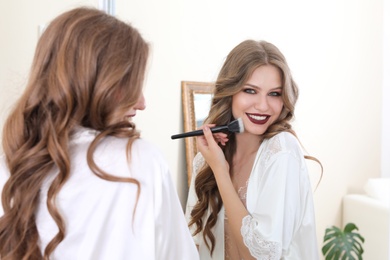 Young woman applying makeup near mirror in dressing room