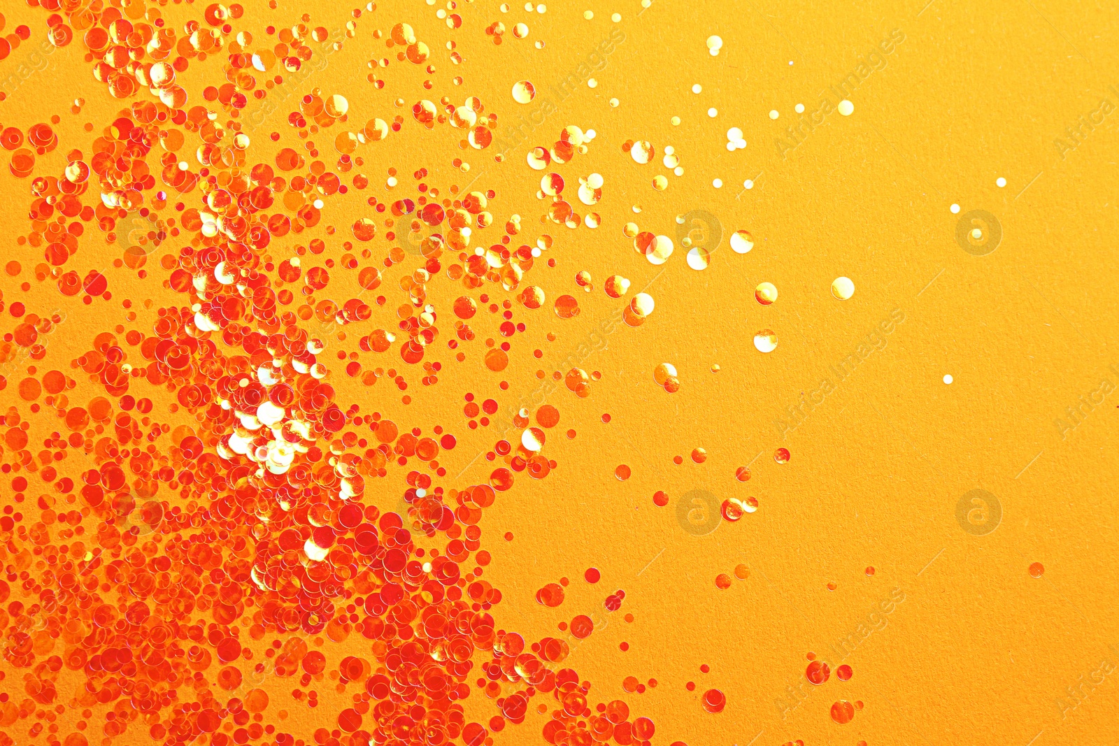 Photo of Shiny bright glitter on orange background, flat lay. Space for text