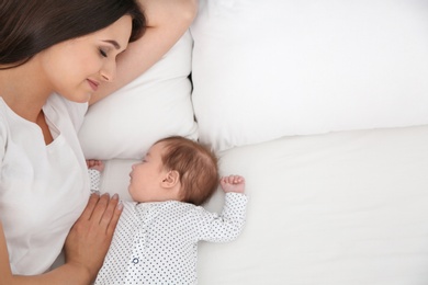 Photo of Woman resting with her sleeping baby on bed. Space for text