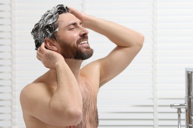 Photo of Happy man washing his hair with shampoo in shower