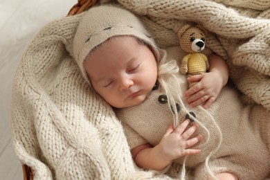 Photo of Adorable newborn baby with toy bear sleeping in basket, top view