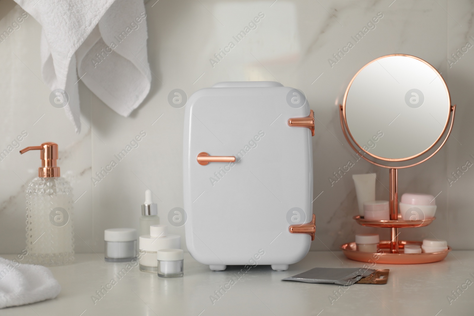 Photo of Cosmetics refrigerator and skin care products on white table indoors