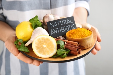 Photo of Woman holding tray with fresh products on grey background, closeup. Natural antibiotics
