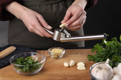 Photo of Woman squeezing garlic with press at wooden table, closeup