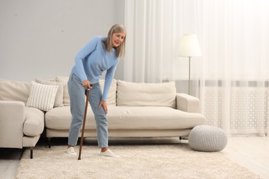 Photo of Mature woman with walking cane suffering from knee pain at home. Rheumatism symptom