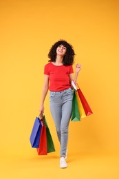 Photo of Happy young woman with shopping bags on yellow background