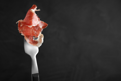 Photo of Tasty prosciutto on fork against grey background. Space for text