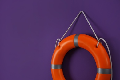 Orange lifebuoy and space for text on violet background. Rescue equipment