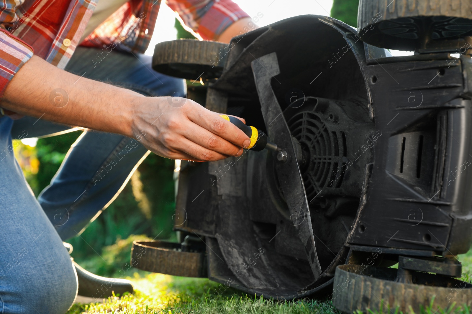 Photo of Man with screwdriver fixing lawn mower outdoors, closeup