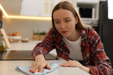 Photo of Woman with microfiber cloth cleaning white marble countertop in kitchen, selective focus