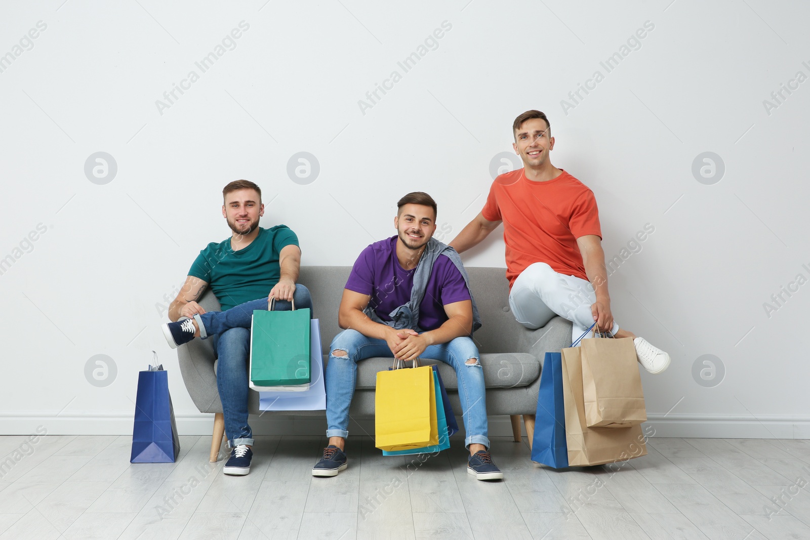 Photo of Group of young men with shopping bags sitting on sofa near light wall