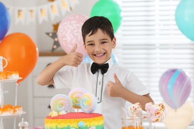 Photo of Happy boy at table with treats in room decorated for birthday party