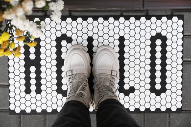 Photo of Woman standing on doormat with word Hello, closeup
