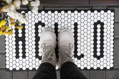 Woman standing on doormat with word Hello, closeup