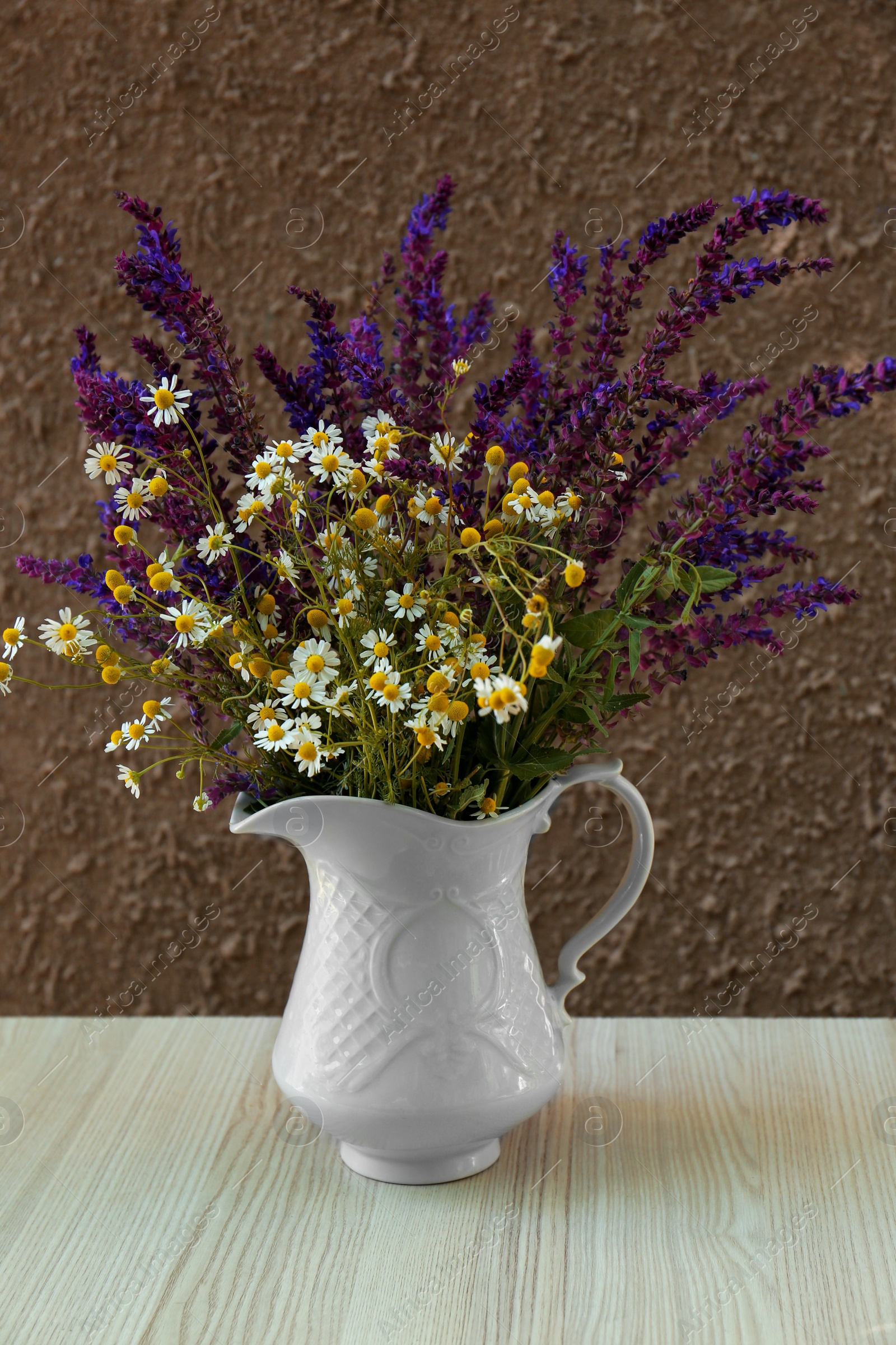 Photo of Beautiful bouquet with field flowers in jug on white wooden table