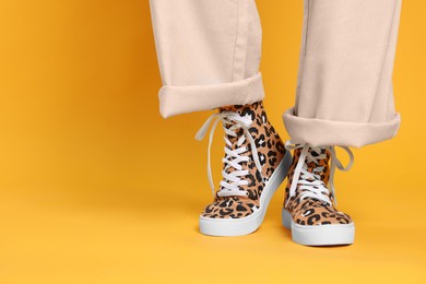 Photo of Woman wearing classic old school sneakers with leopard print on orange background, closeup. Space for text
