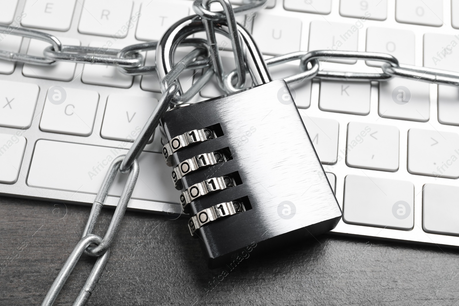 Photo of Cyber security. Metal combination padlock with chain and keyboard on grey table, closeup