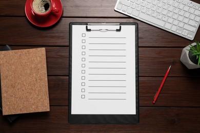 Photo of Clipboard with checkboxes, cup of coffee, plant and computer keyboard on wooden table, flat lay. Checklist