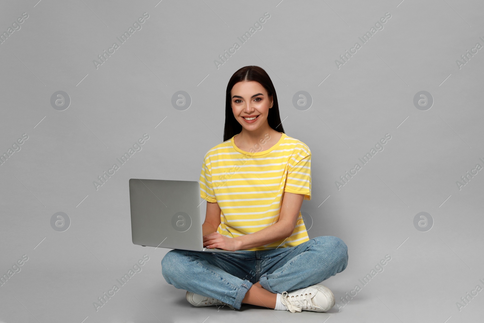 Photo of Young woman with modern laptop on light grey background. Space for text