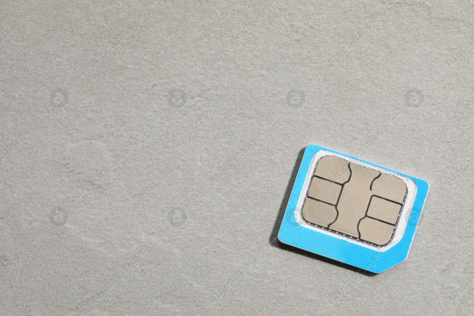 Photo of Micro SIM card on light grey stone background, top view. Space for text