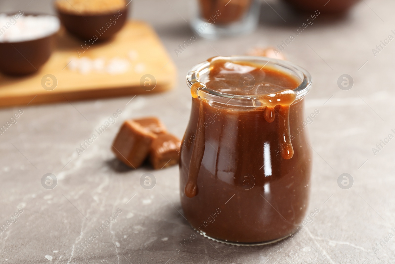 Photo of Jar with tasty caramel sauce on grey table. Space for text