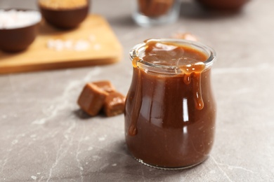 Photo of Jar with tasty caramel sauce on grey table. Space for text