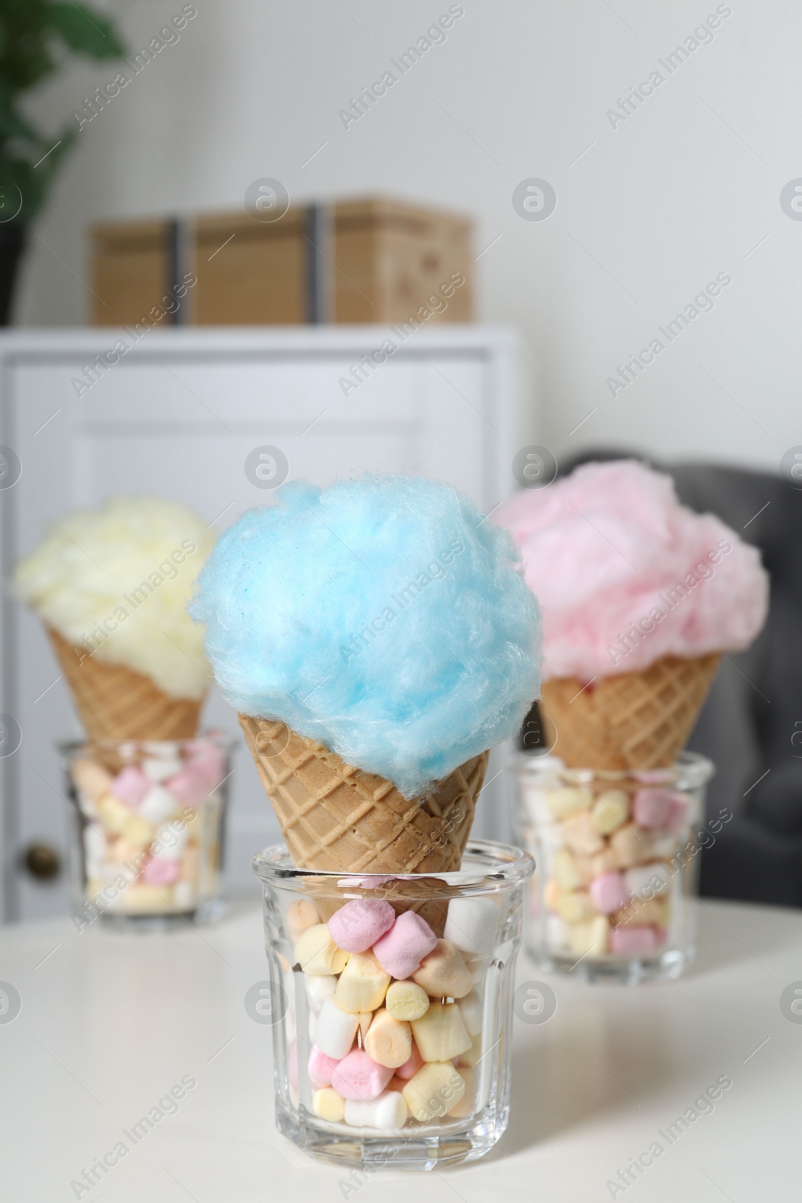 Photo of Sweet cotton candies in waffle cones and marshmallows on white table indoors, closeup