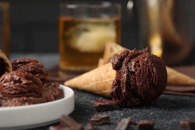 Photo of Tasty ice cream scoops, chocolate crumbs and waffle cones on dark textured table, closeup
