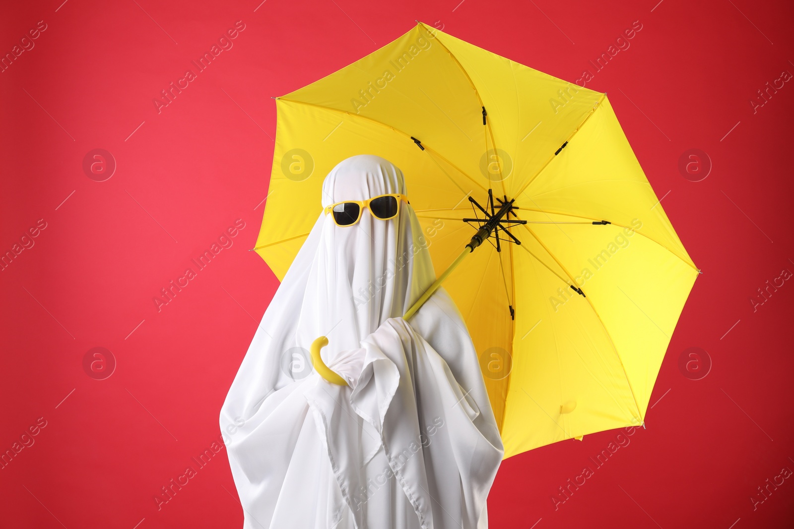 Photo of Person in ghost costume and sunglasses holding yellow umbrella on red background