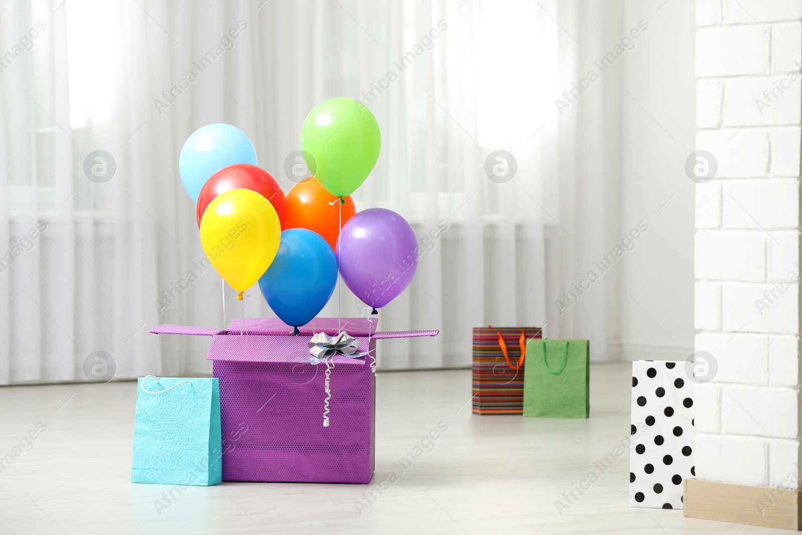 Photo of Gift box with bright air balloons on floor indoors. Space for text