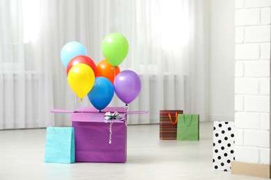 Gift box with bright air balloons on floor indoors. Space for text